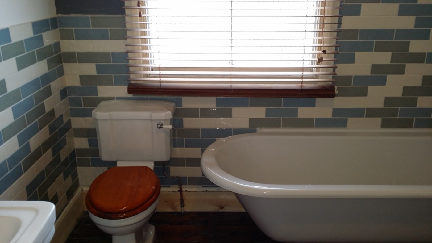 Roll-top bath beside blue, green and white brick tiles
