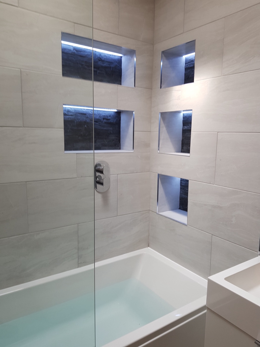 Bath and shower wall with illuminated slate-lined storage niches